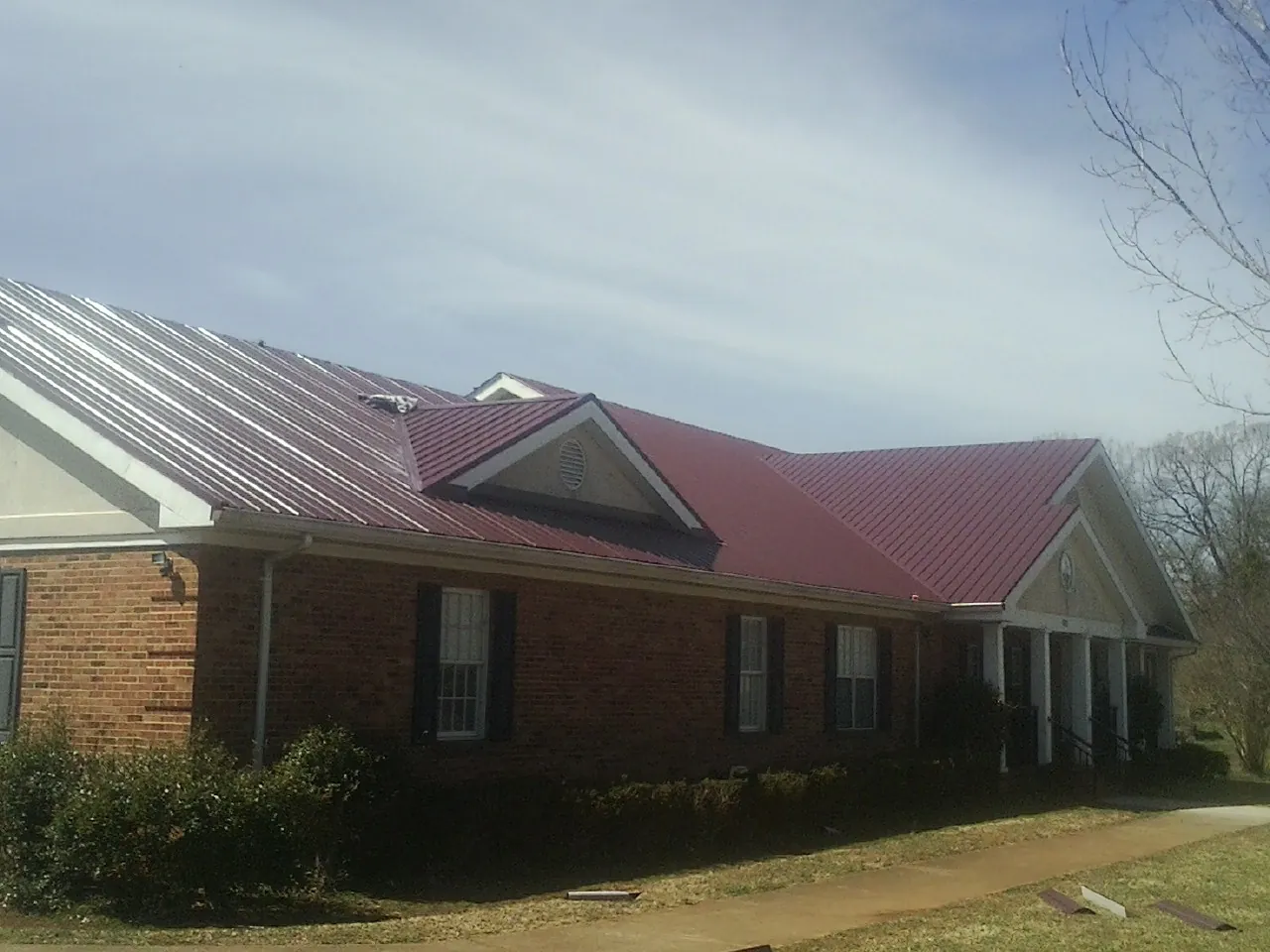 Red metal roof with gabled entries on a long brick building, from a Hail Damage Roof Repair job in West Haverstraw
