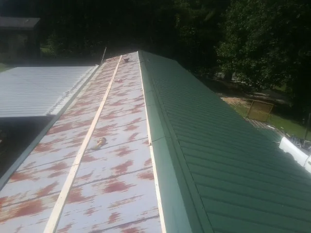 Old rusted panels beside newly installed green metal roofing — Wind Damage Roof Repair by Roofing Brothers in West Haverstraw