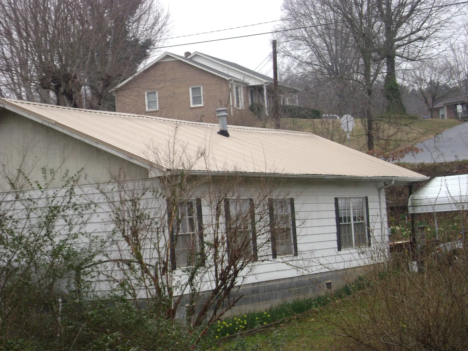 Tan metal roof on a white sided house set into a hillside — Commercial Roofing by Roofing Brothers in West Haverstraw